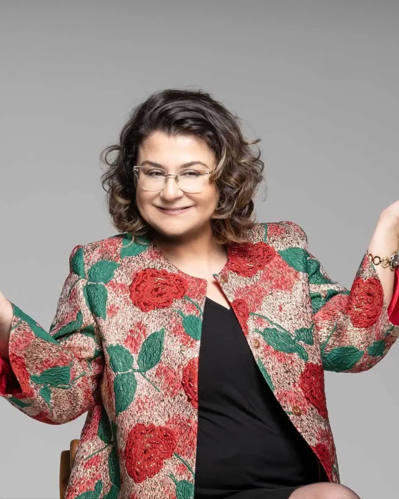 Dr. Menekşe Ahbab, çiçek desenli ceketle elleri açık konuşurken