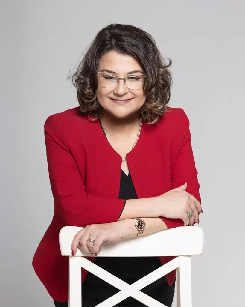 Dr. Menekşe Ahbab, kırmızı ceketle stüdyoda sandalyeye yaslanmış